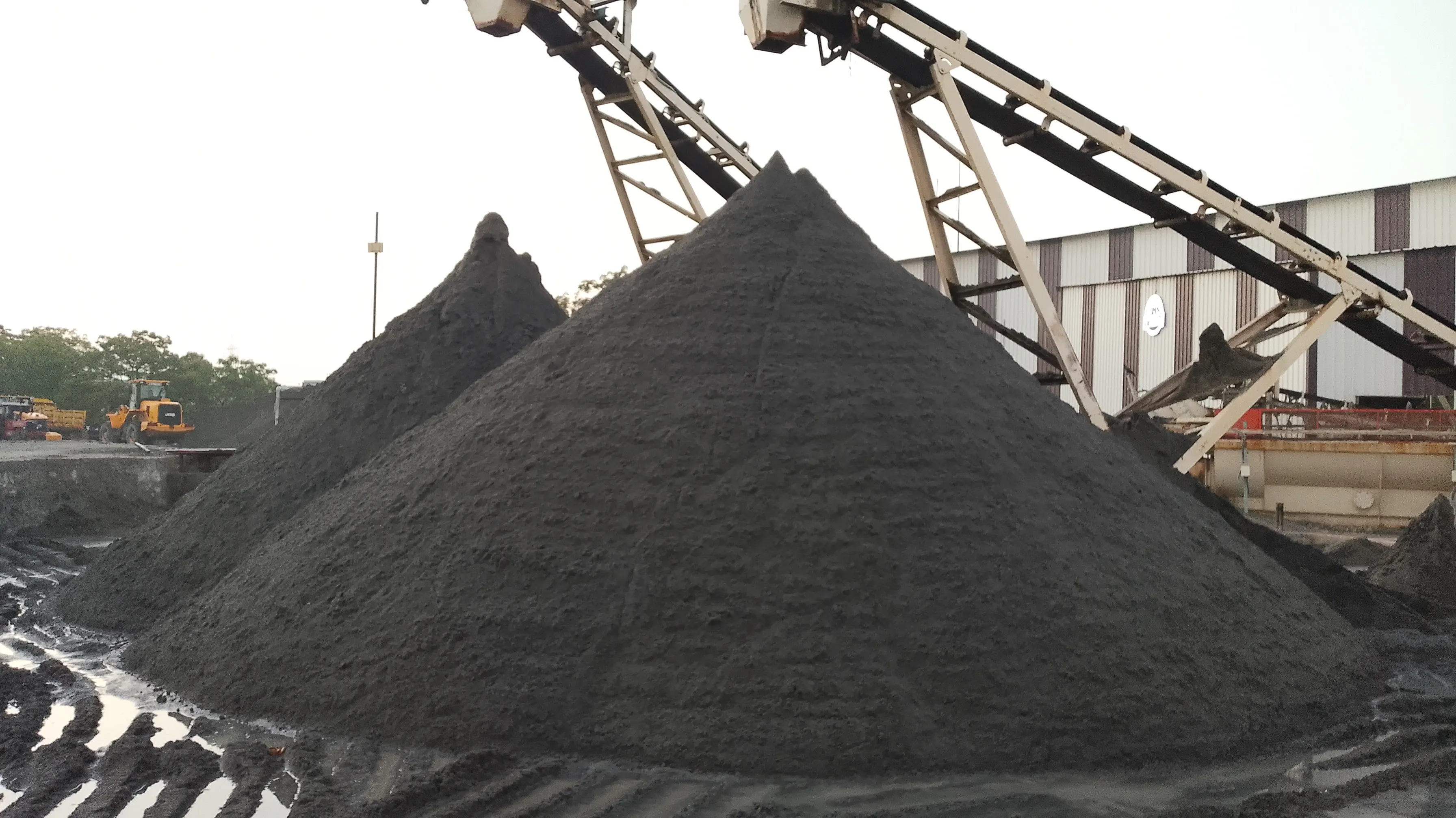 Large Manufactured Sand (M-Sand) stockpiles under conveyor belts in daylight at Tirupati Balaji Blue Metals LLP, Virudhunagar, Tamil Nadu